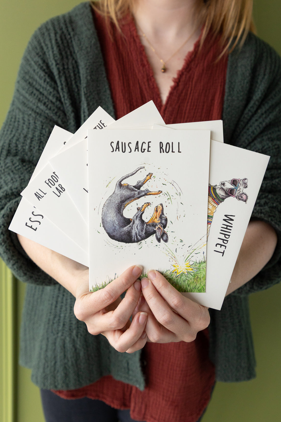Person holding a stack of greeting cards with dog illustrations and text.