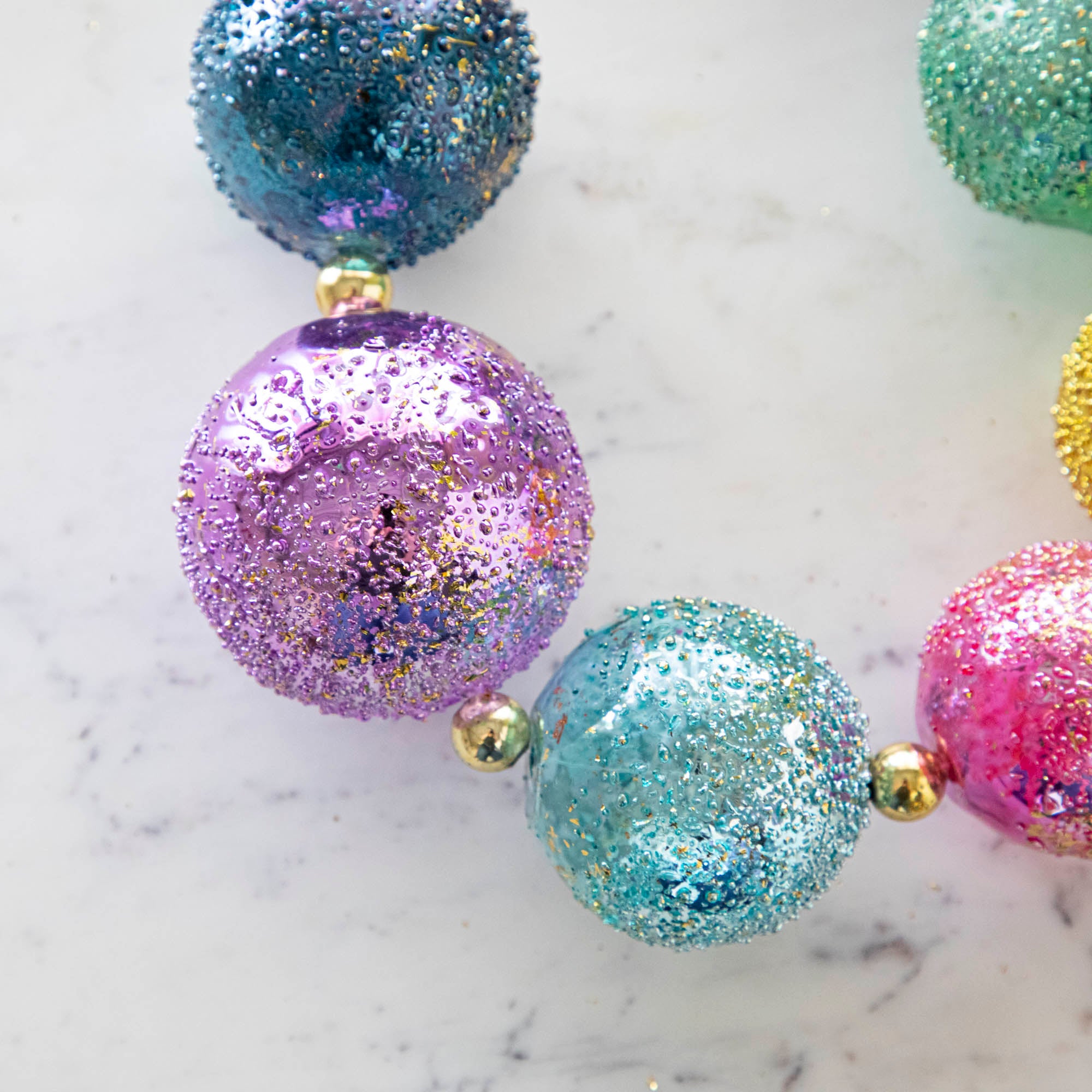 Close up of a colorful shiny stubble ball garland on a marble table.