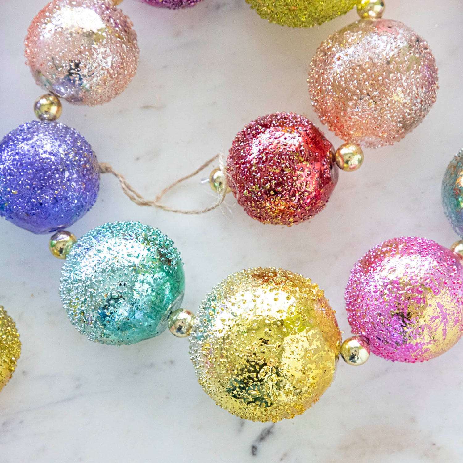 Close up of colorful shiny stubble ball garland on a marble table.