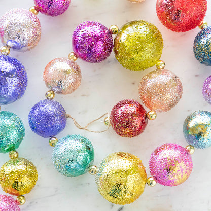 Close up of colorful shiny stubble ball garland on a marble table.