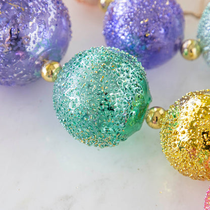 Close up of a turquoise shiny stubble ball garland on marble table.