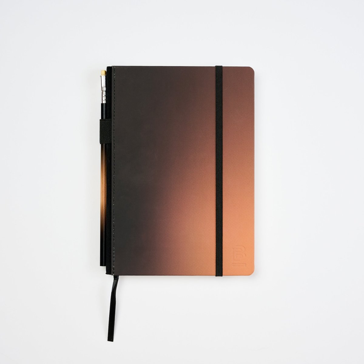 A hardcover notebook with a dark brown to copper-orange gradient cover, featuring a black elastic closure band, a black bookmark ribbon, and a pen tucked into the side pocket, set against a plain white background.