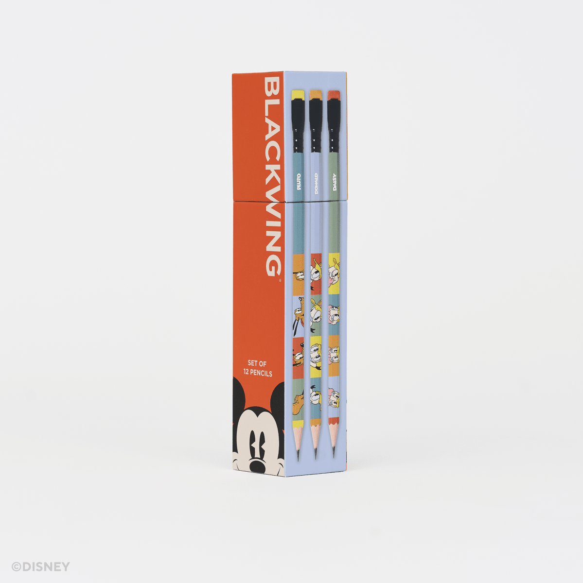A boxed set of three pencils standing upright on a clean white studio background. The packaging is bright orange on the left with the word BLACKWING in large white letters and a Mickey Mouse face at the bottom, while the right side is light blue and shows the pencil barrels with cartoon graphics.