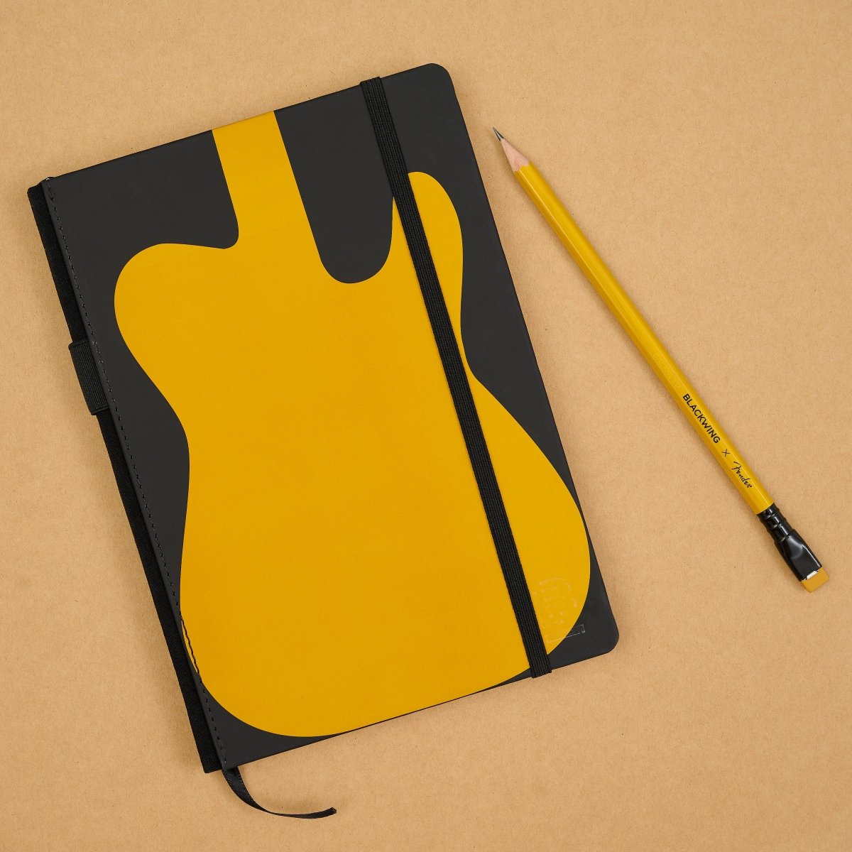 A black notebook with a large yellow guitar-shaped graphic on the cover, shown on a tan background next to a yellow pencil.