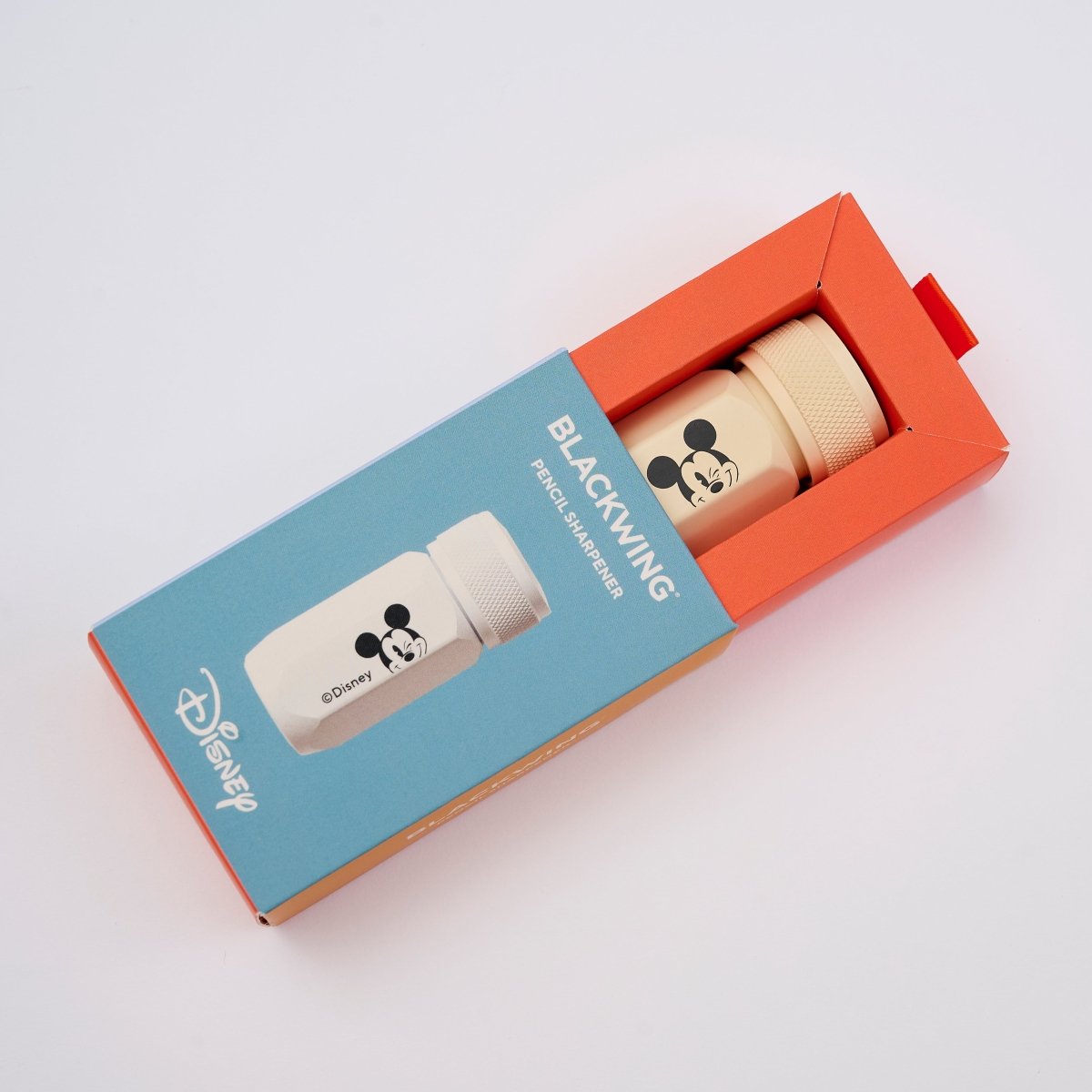 Disney Blackwing Pencil Sharpener in its retail packaging, featuring a light blue and orange box with the cream colored sharpener coming out of the box.