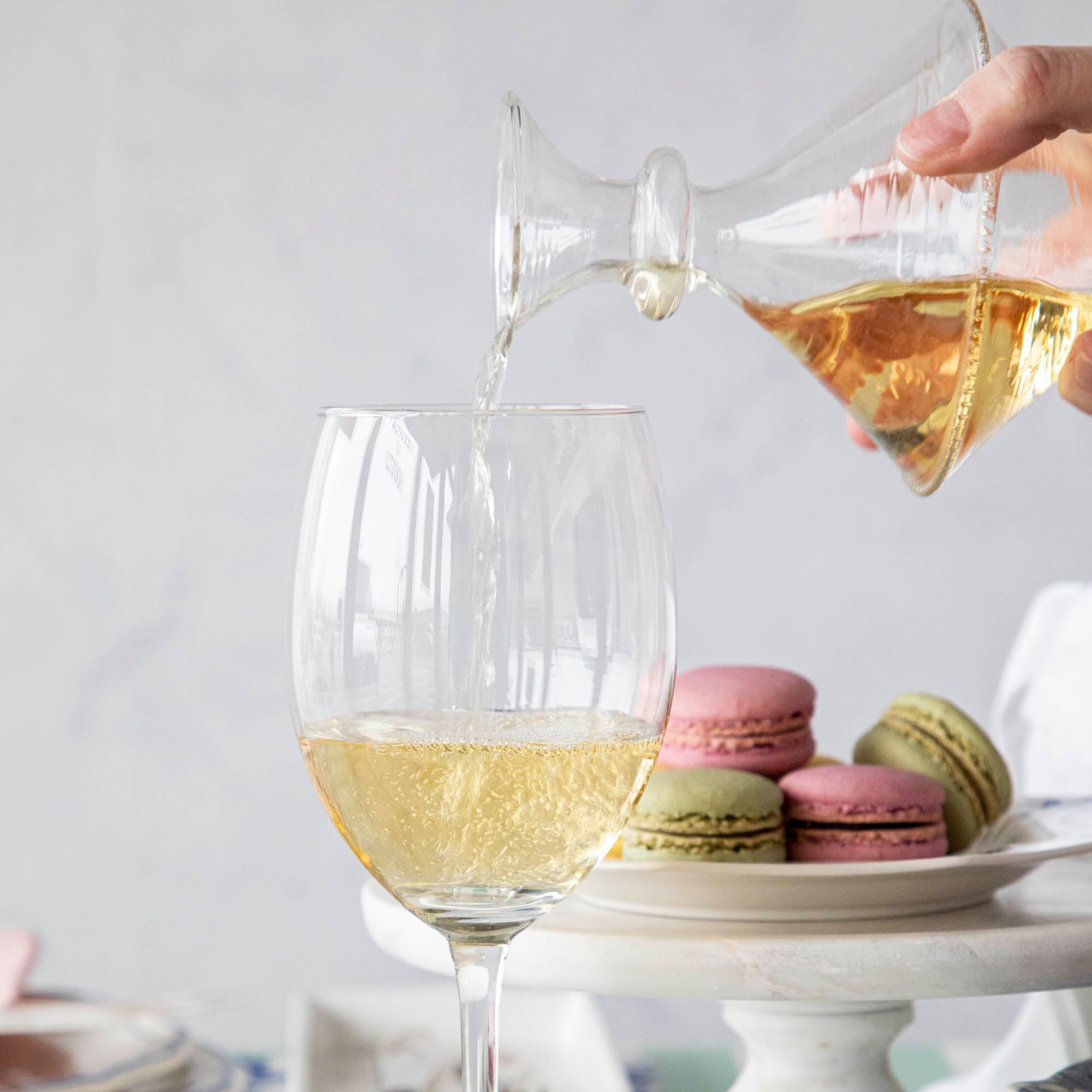 A person pouring white wine into a glass with macarons and placing small bouquets in Qualia Mouth Blown Clear Vases - Exclusively at Hester &amp; Cook.