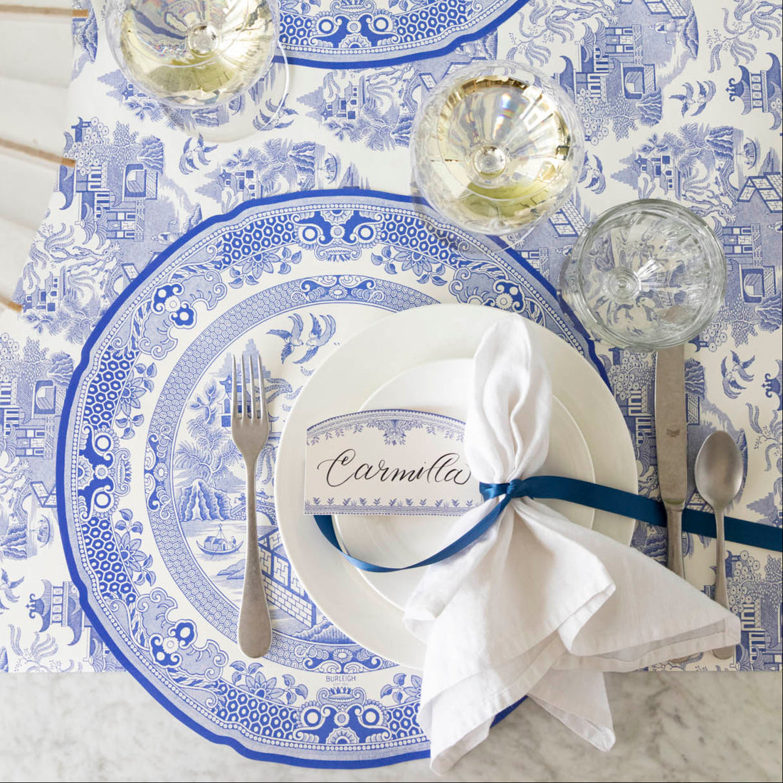 Burleigh Blue Place Card with &quot;Camilla&quot; written in the white space, resting on dinner plates, on top of the Die-cut Blue Willow Plate Placemat. 