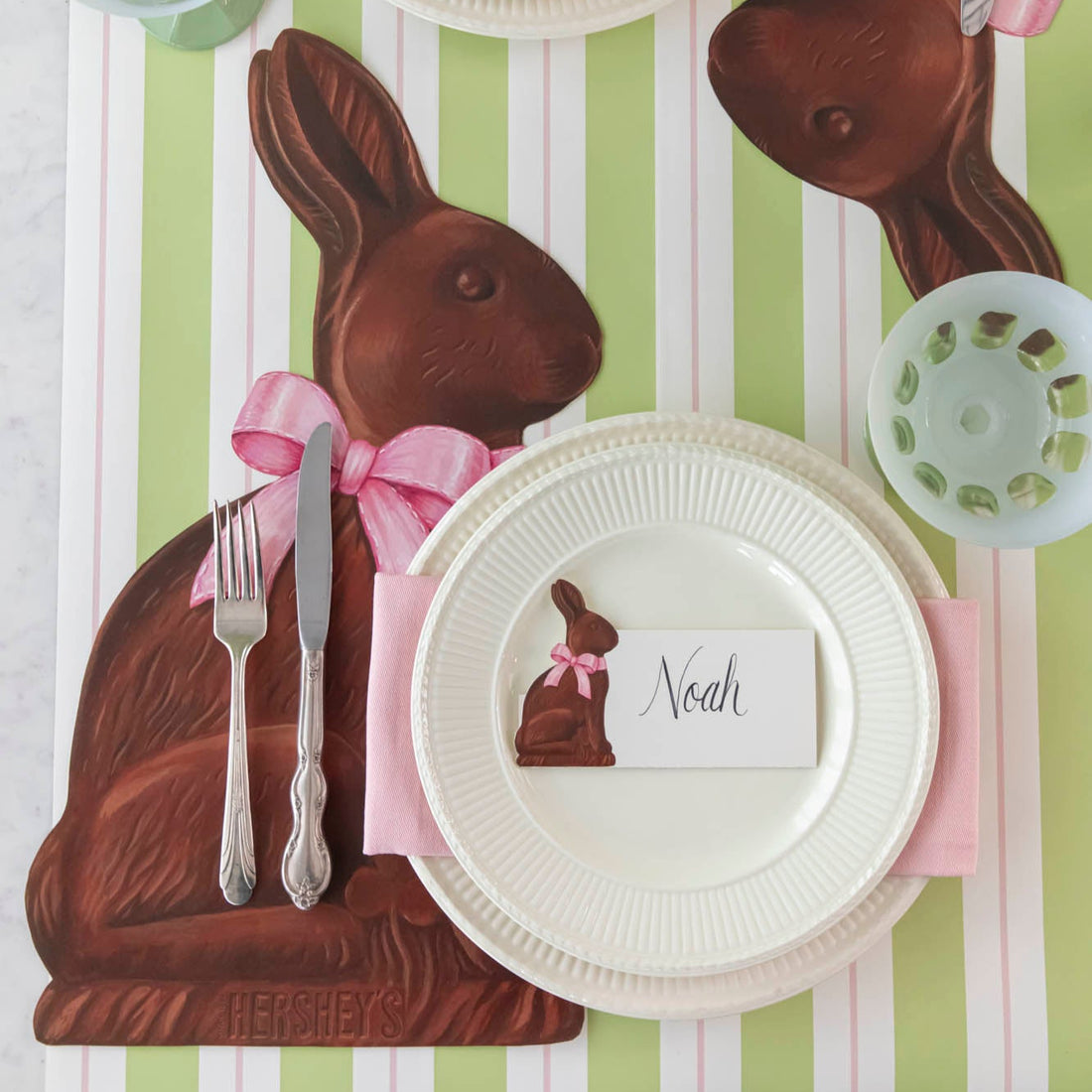 Easter-themed place setting with Hershey's chocolate bunny, white plate, and name card on a striped background.
