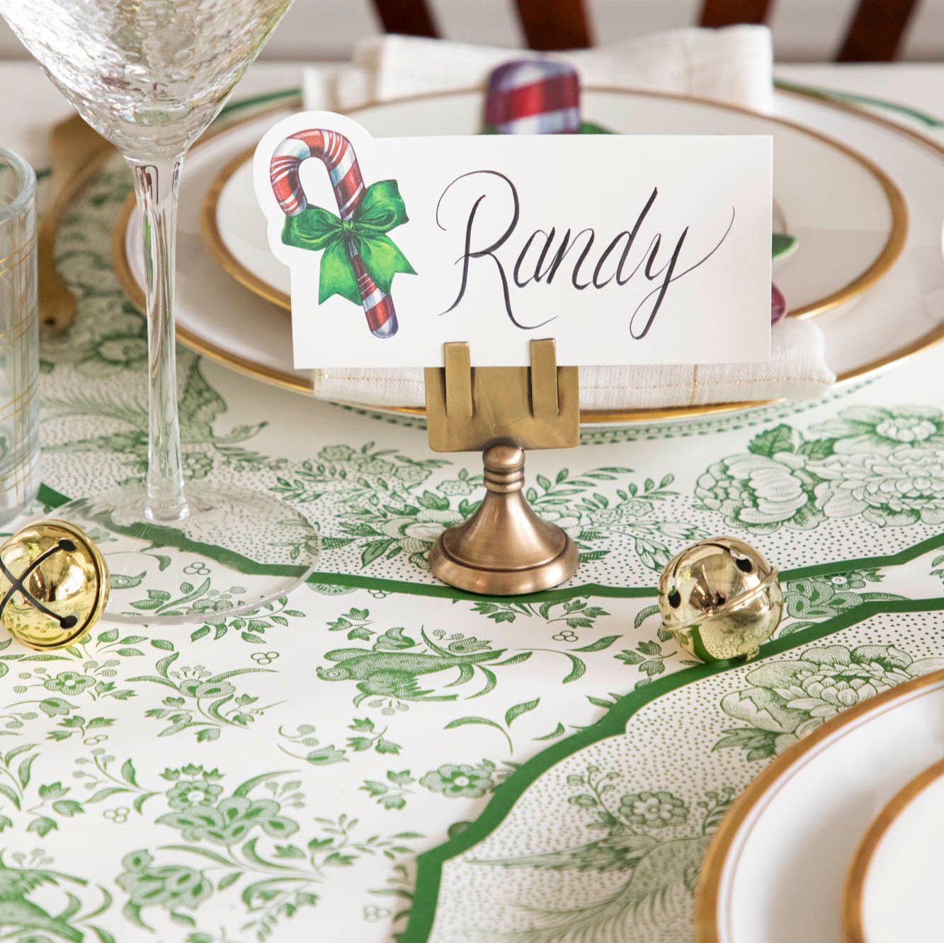 An elegant table setting featuring the Candy Cane Place Card with &quot;Randy&quot; written on it, held up by the Brass Place Card Holder.