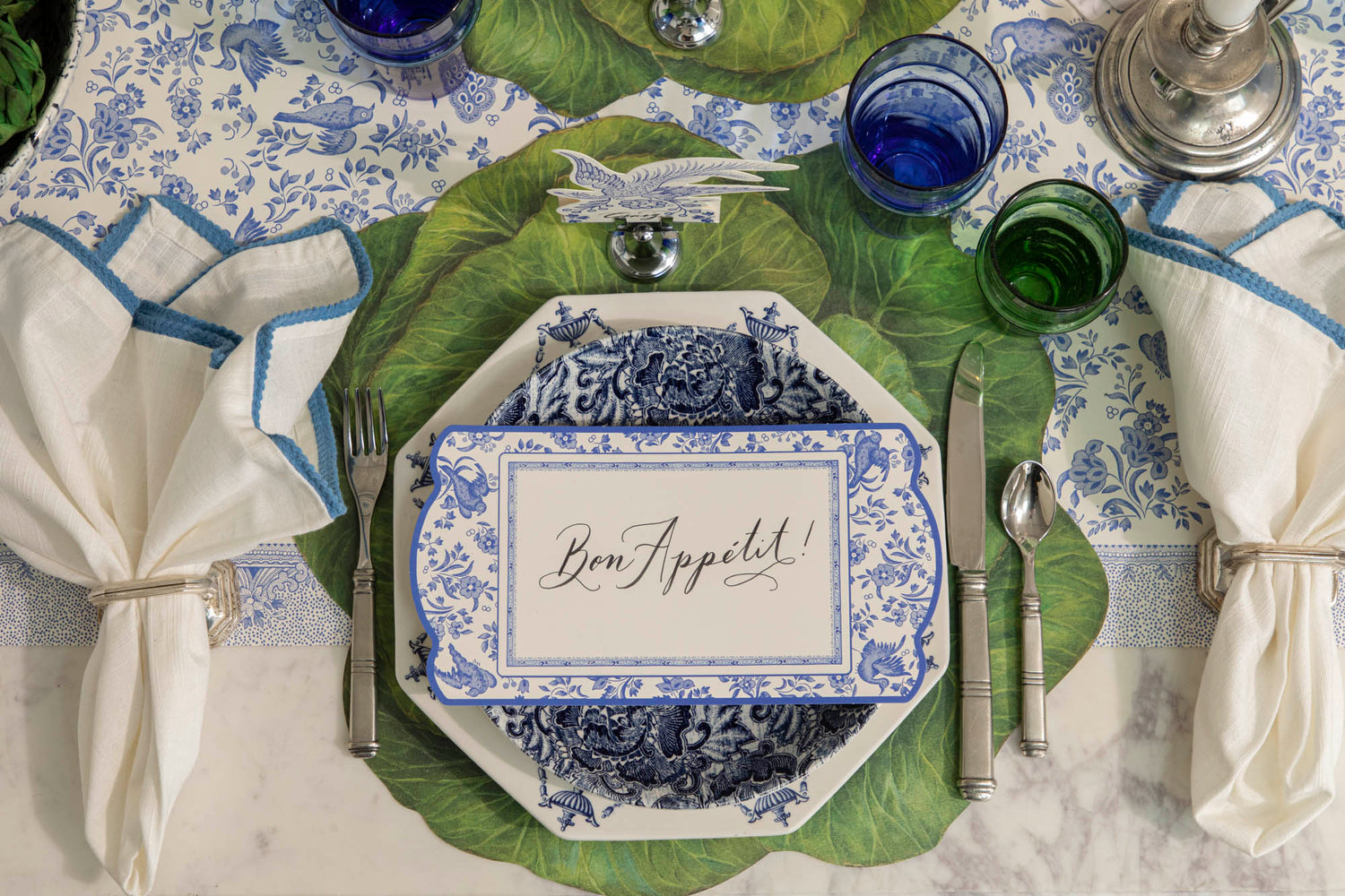 Dining table set with decorative blue plates, vintage cutlery, green and blue glasses and napkins on the Die-cut Cabbage Placemat and Blue Regal Peacock Runner.