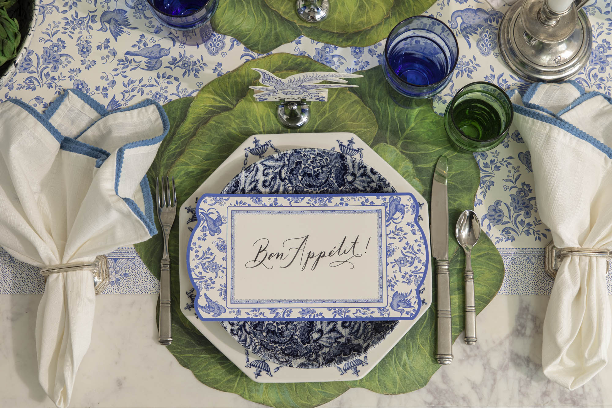 Dining table set with decorative blue plates, vintage cutlery, green and blue glasses and napkins on the Die-cut Cabbage Placemat and Blue Regal Peacock Runner.