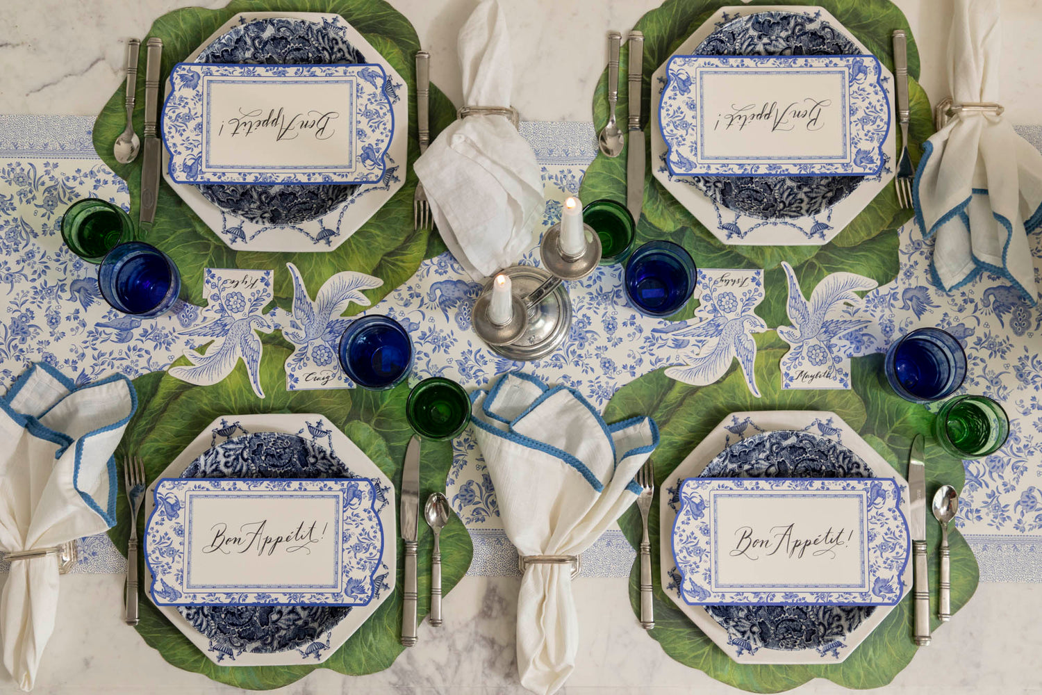 Dining table set with decorative blue plates, vintage cutlery, green and blue glasses and napkins on the Die-cut Cabbage Placemat and Blue Regal Peacock Runner.