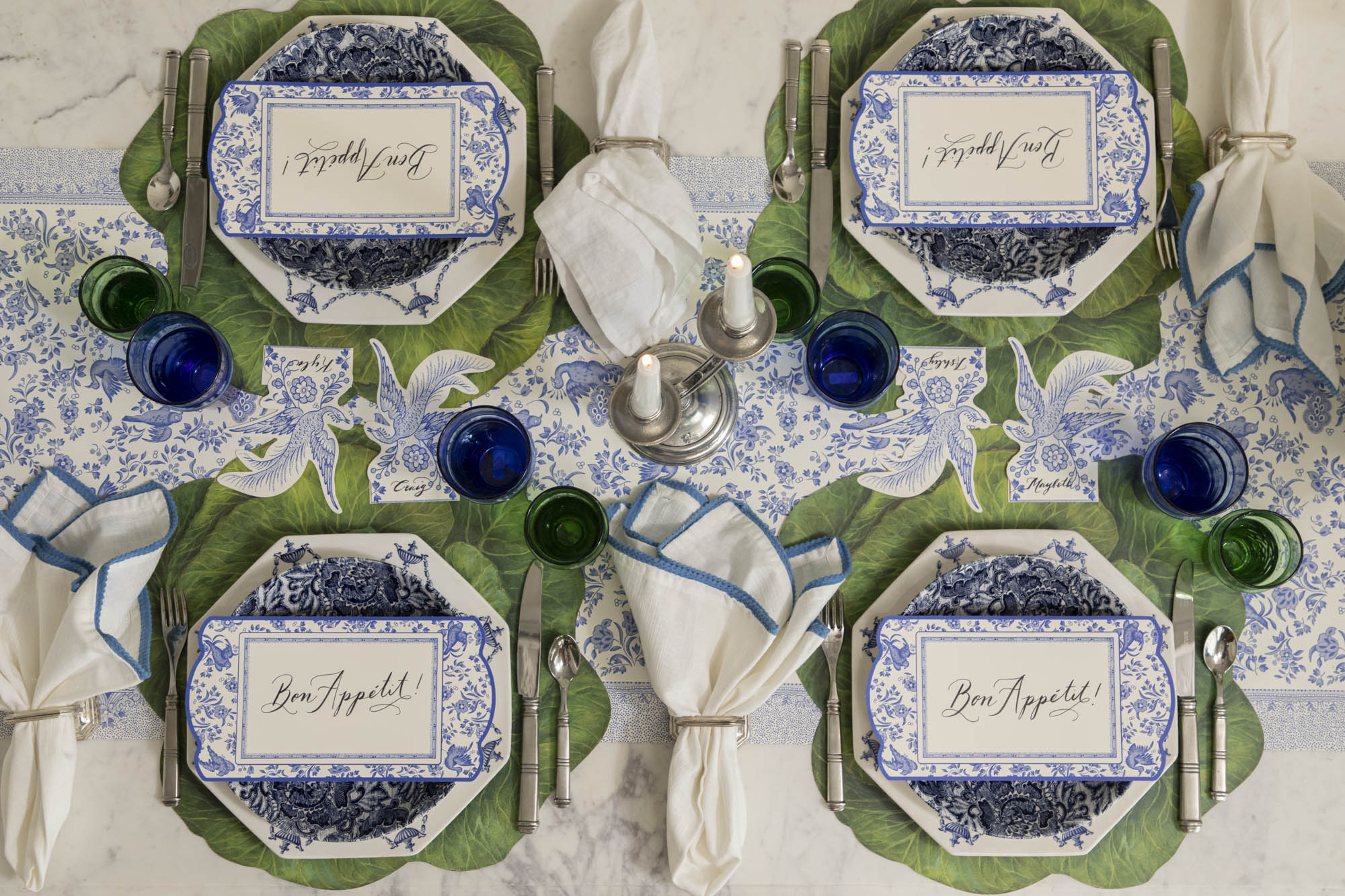 Dining table set with decorative blue plates, vintage cutlery, green and blue glasses and napkins on the Die-cut Cabbage Placemat and Blue Regal Peacock Runner.