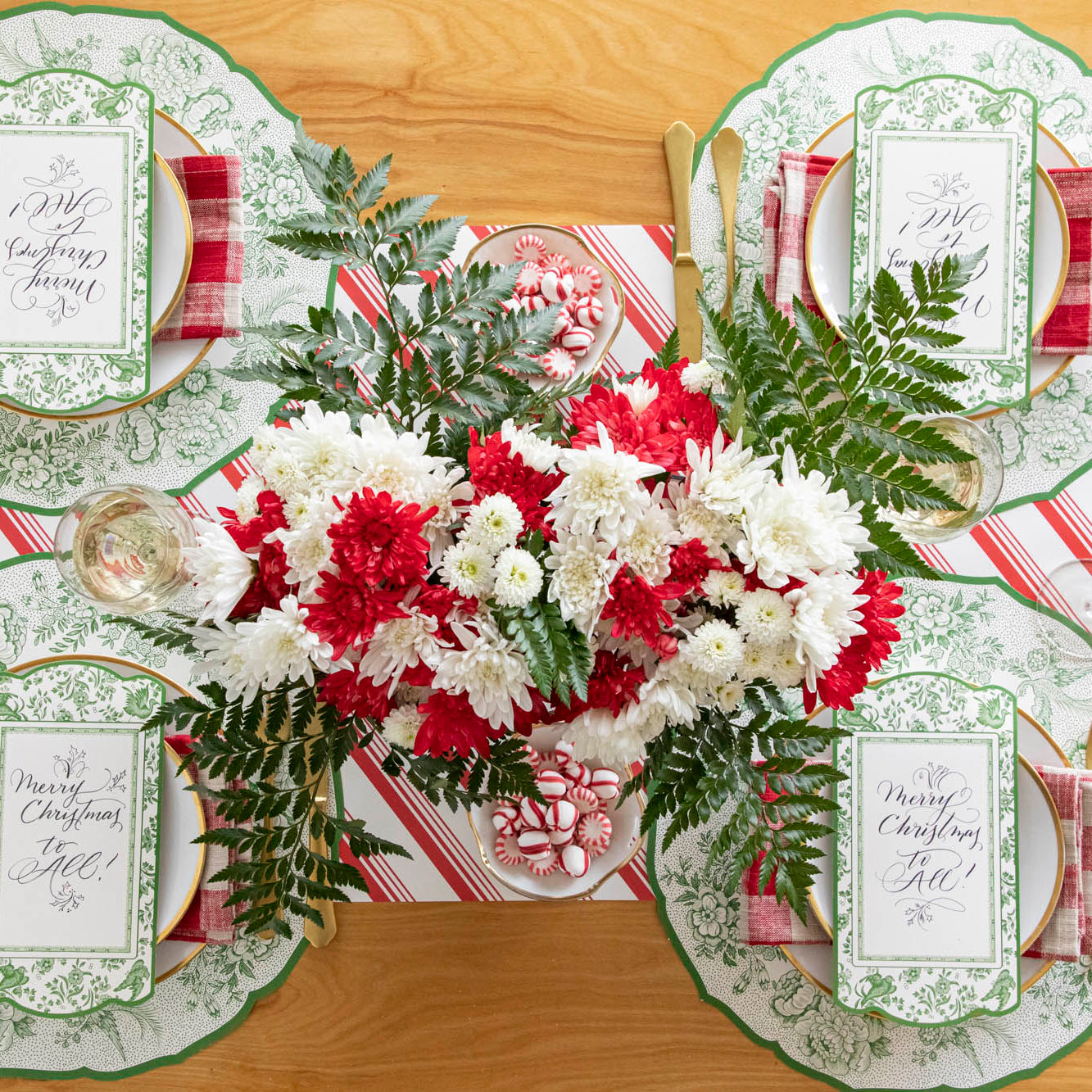 A Christmas table setting featuring a winter floral centerpiece, Die-cut Green Asiatic Pheasants Placemats and table cards and gold rimmed plates on the Peppermint Stripe Runner.