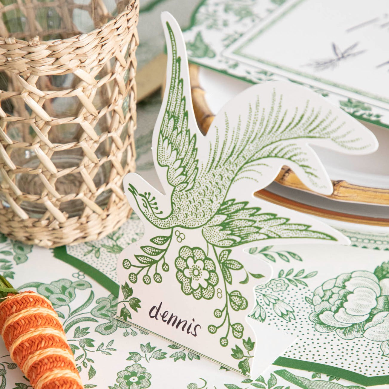 A Green Asiatic Pheasants Place Card designed by Hester &amp; Cook, featuring a bird and carrots, is placed to make guests feel welcomed.