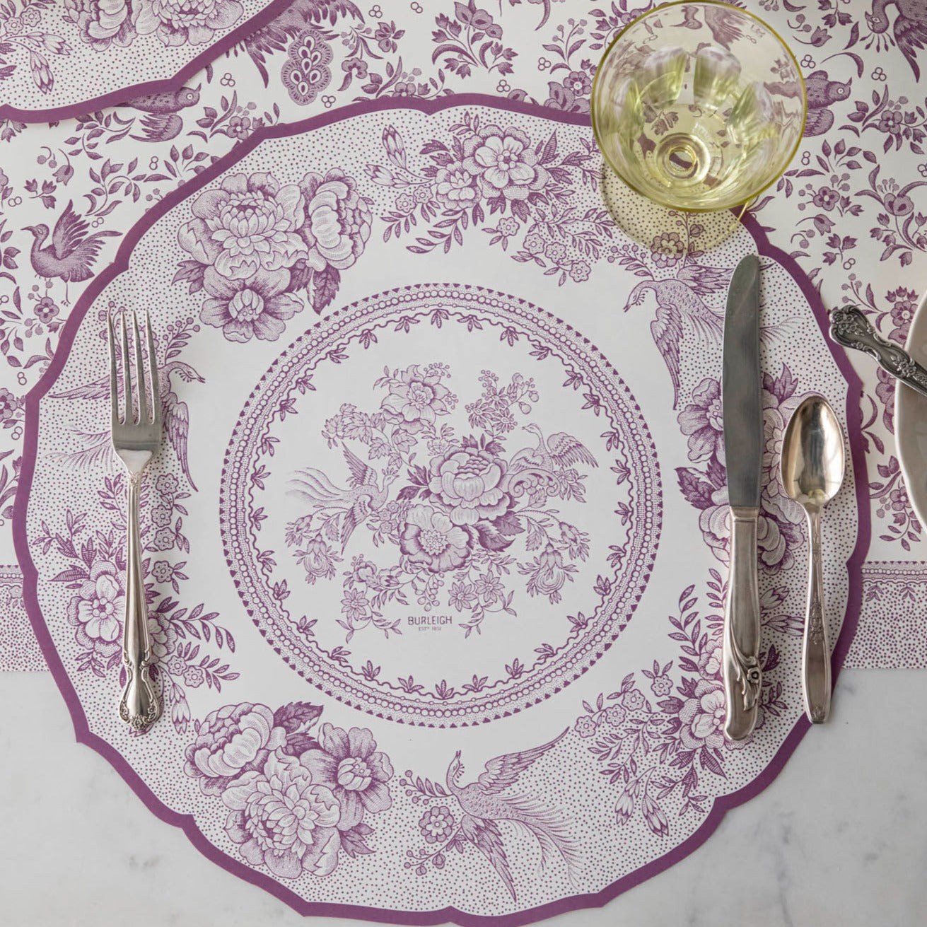 A purple and white tablescape with the Hester &amp; Cook Die-cut Lilac Asiatic Pheasants Placemats, silverware, and utensils.