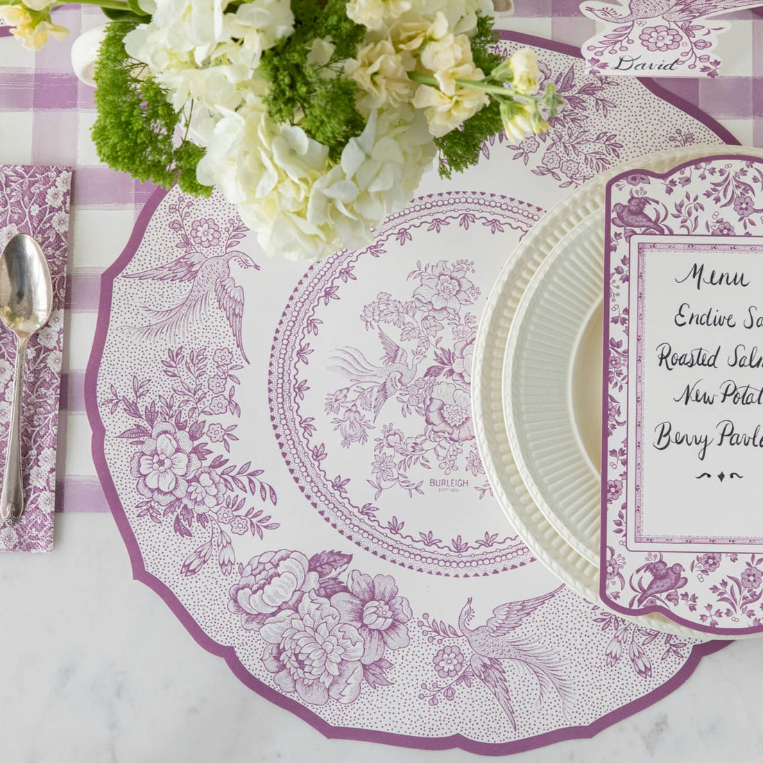 A tablescape featuring a purple and white tablecloth adorned with the Hester &amp; Cook Die-cut Lilac Asiatic Pheasants Placemats.