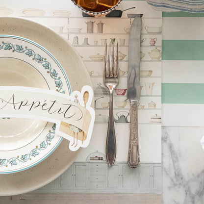 Two Cooks Banner Table Accent with &quot;Bon Appetit&quot; written on it, resting on dinner plates, on an elegant place setting for one.