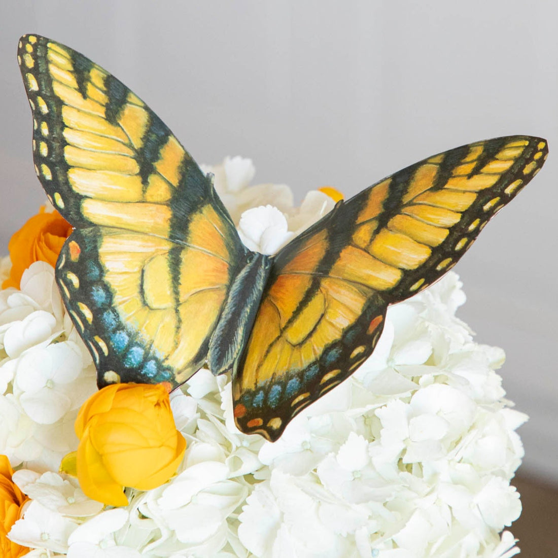 Close-up of the yellow Butterfly Table Accent, wings folded up slightly, resting on a bouquet of white flowers.