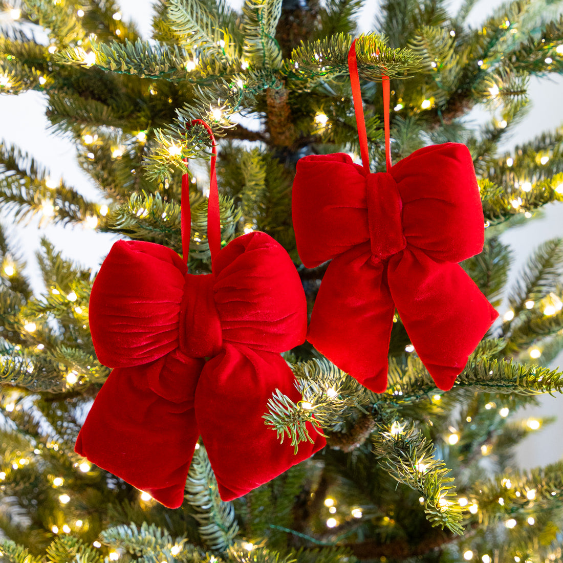 Red velvet bows hanging on a decorated Christmas tree.