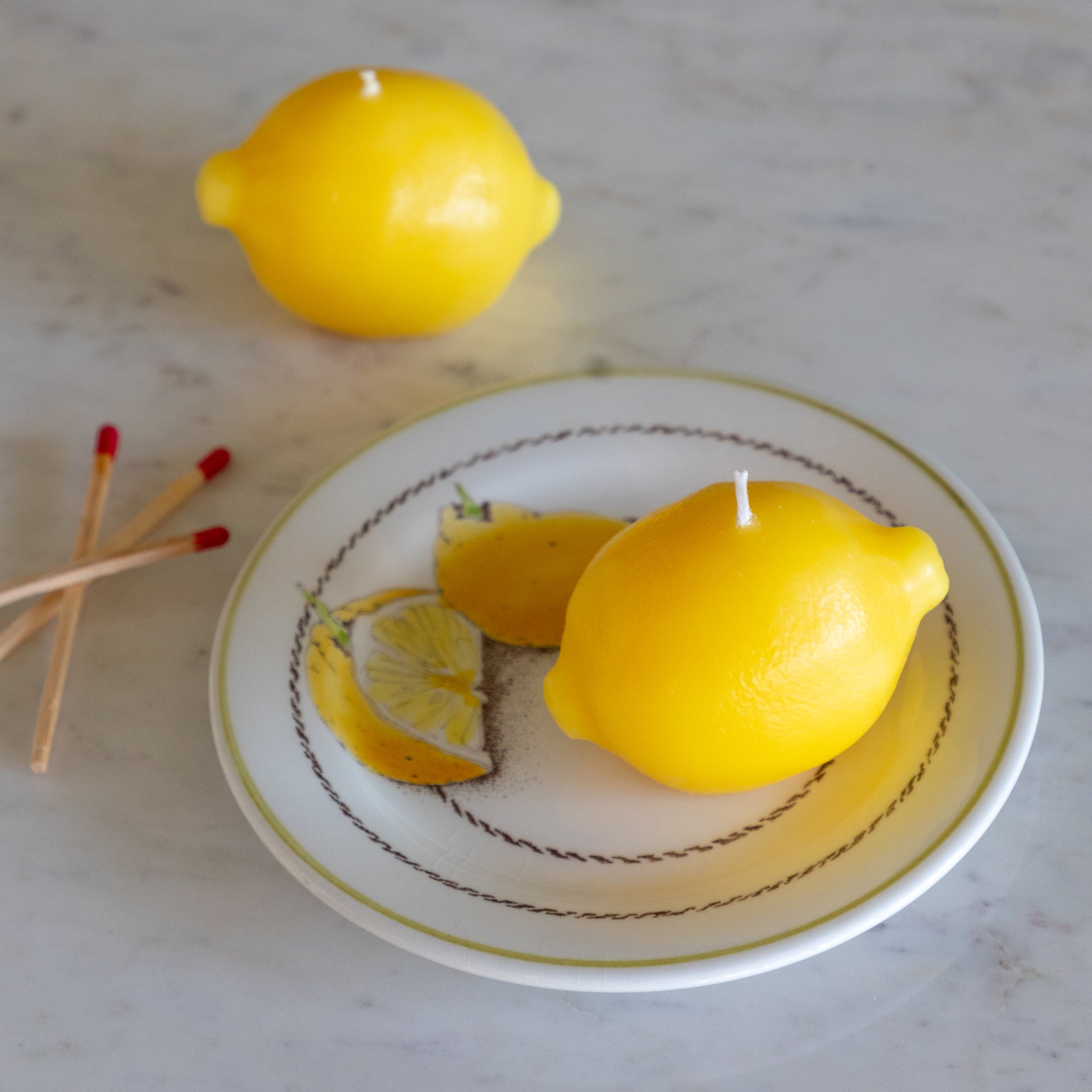 Lemon-shaped candles on a decorative plate with matches on a marble surface.