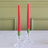 Two Watermelon Taper Candles in clear candle holders on a marble surface with a green wall background.