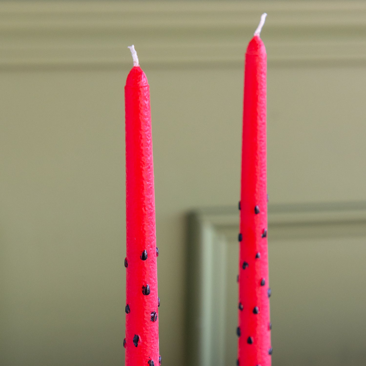 Two Watermelon Taper Candles on a green wall background.
