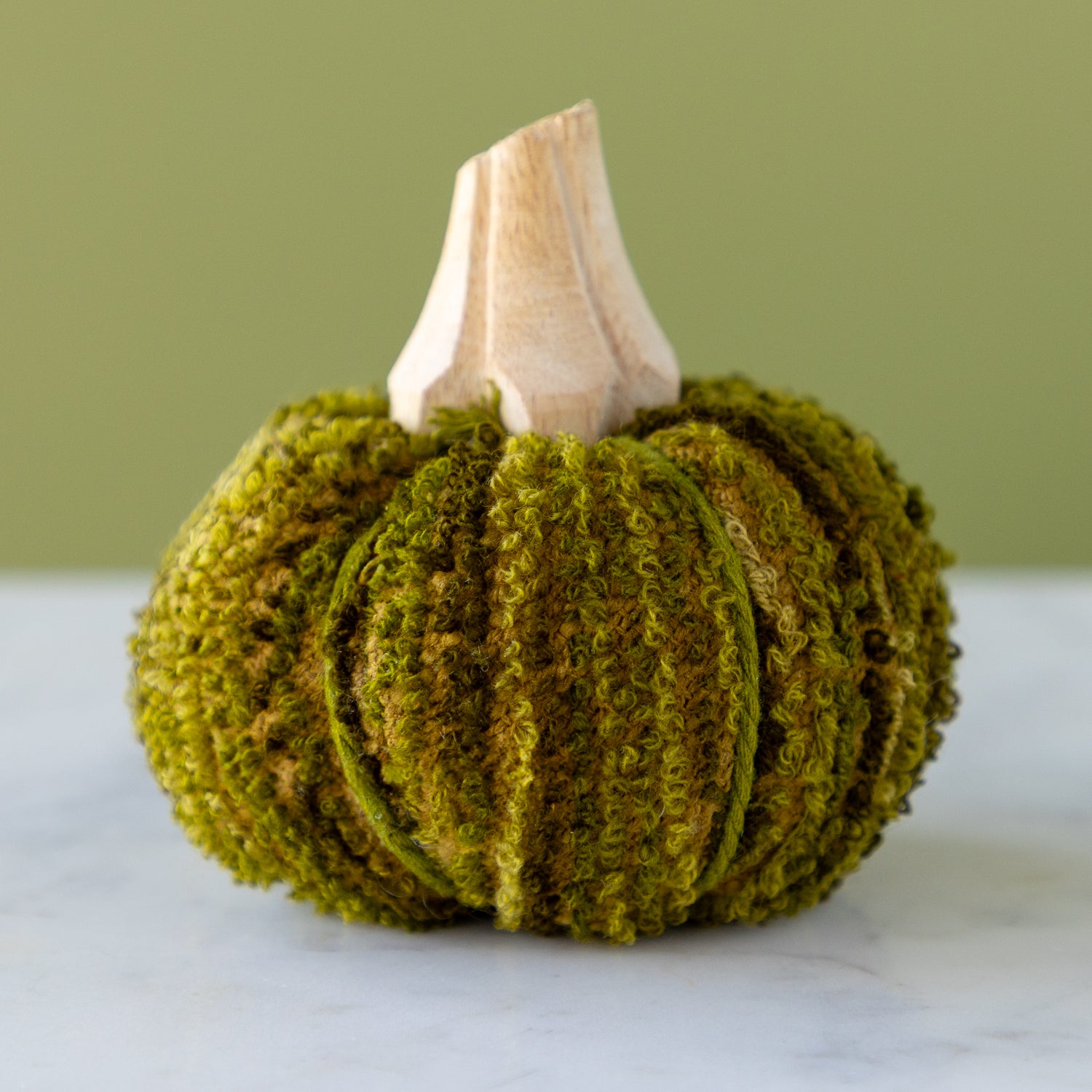 Moss-colored, cotton blend bouclé/velvet pumpkin with a wooden stem on a marble table.
