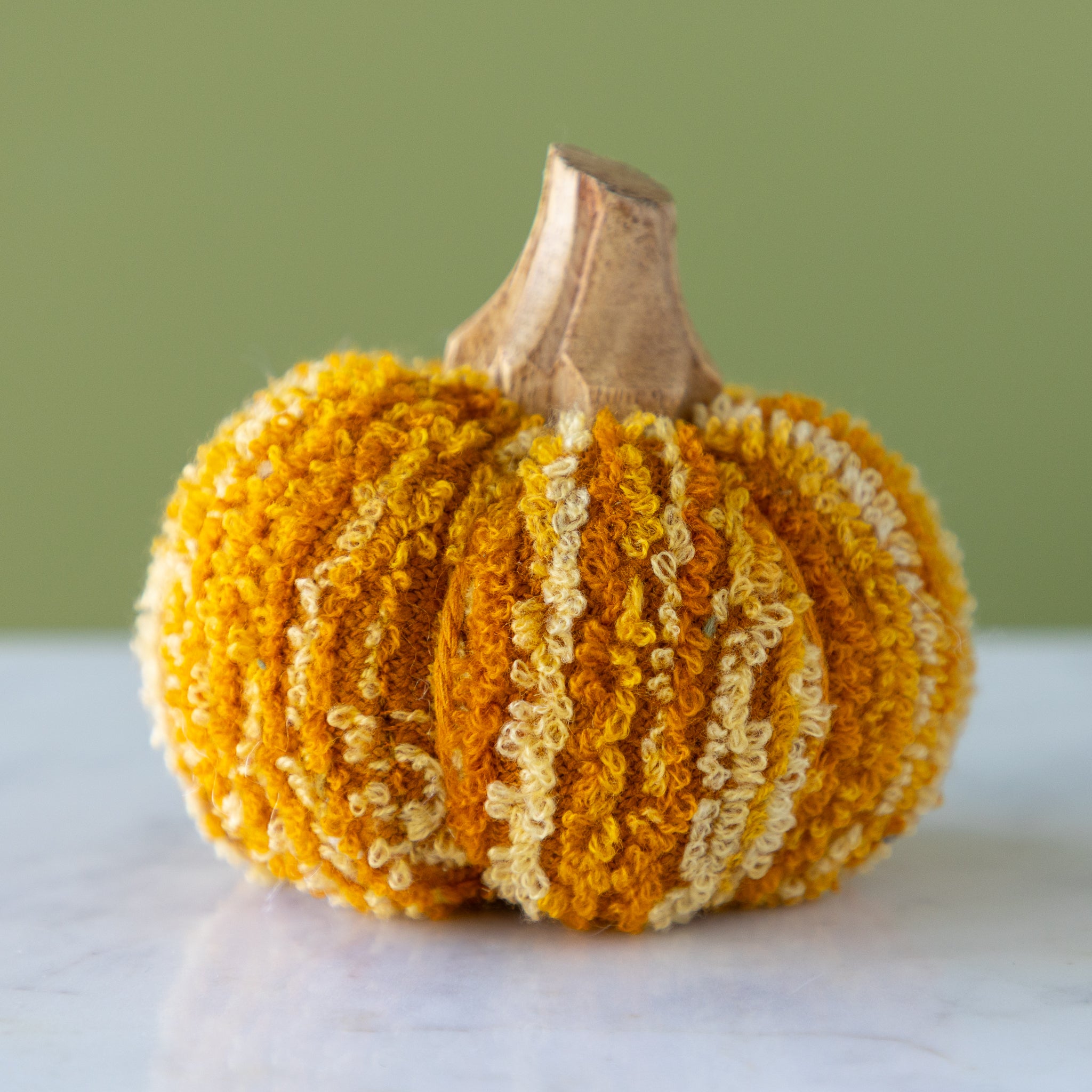 Marigold-colored, cotton blend bouclé/velvet pumpkin with a wooden stem on a marble table.