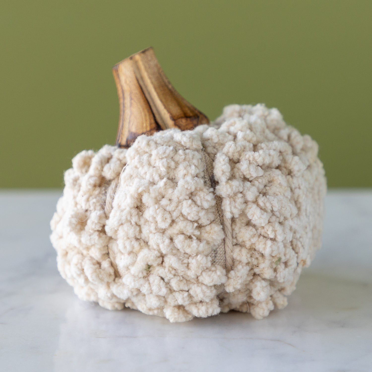 White, cotton blend bouclé/velvet pumpkin with a wooden stem on a marble table.