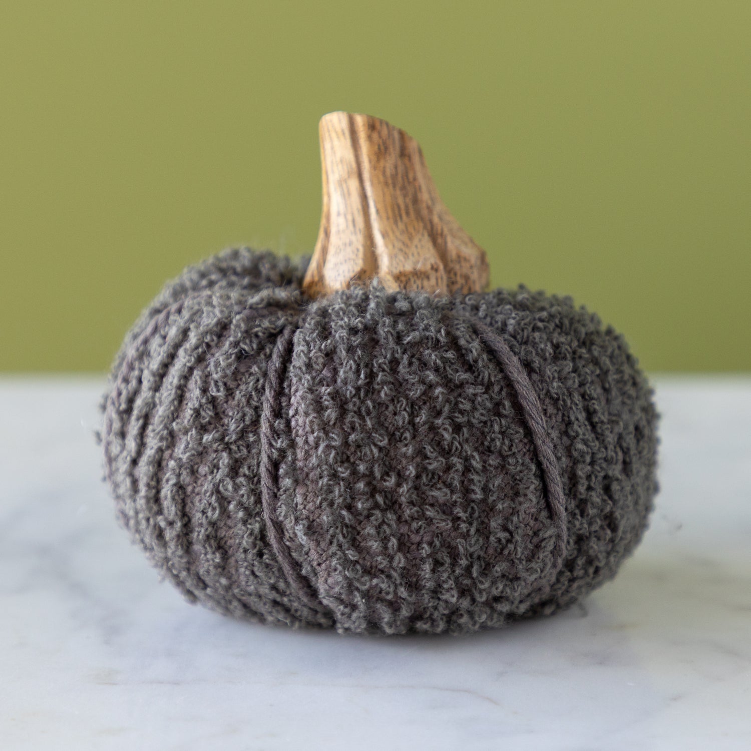 Slate bouclé  pumpkin with a wooden stem on a marble table.
