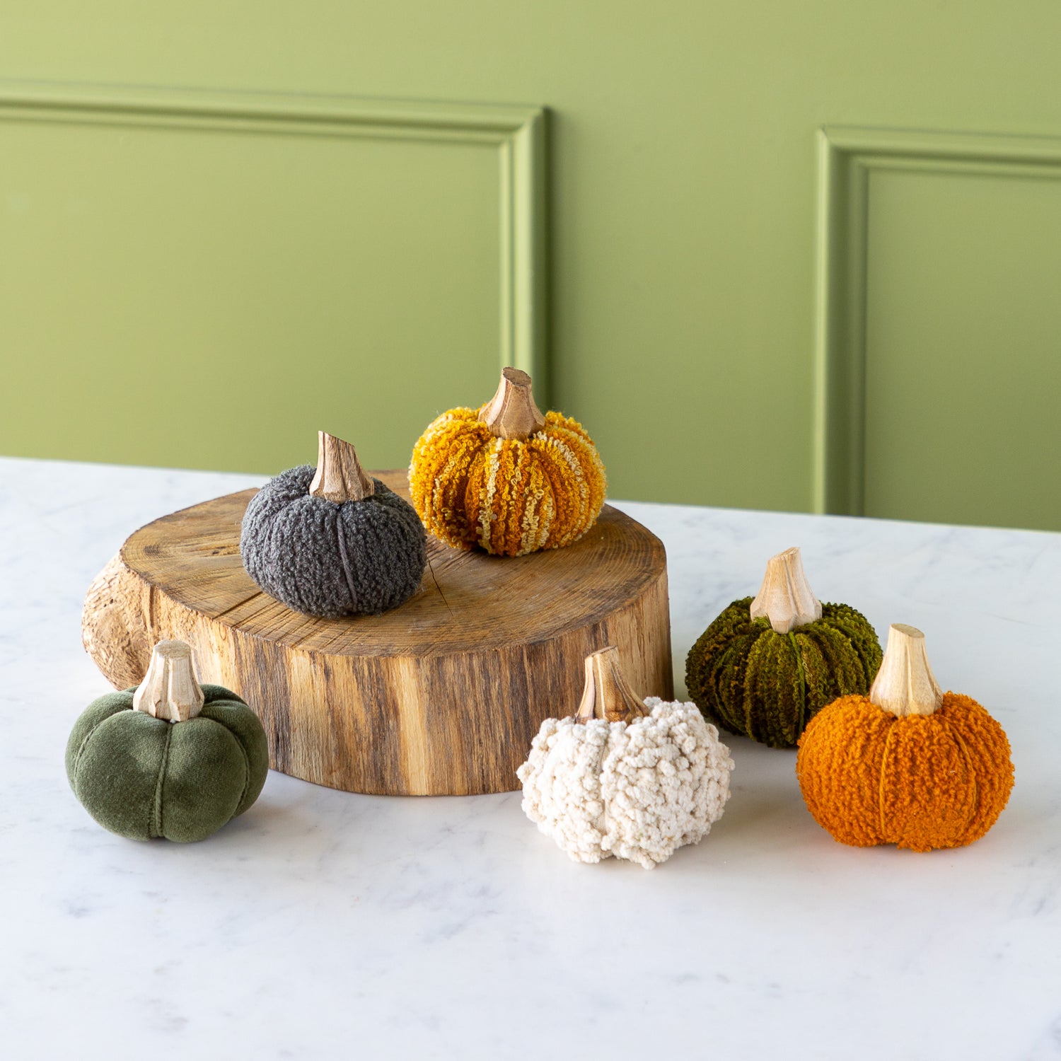 Knitted pumpkins in various colors on a wooden stand against a green wall.