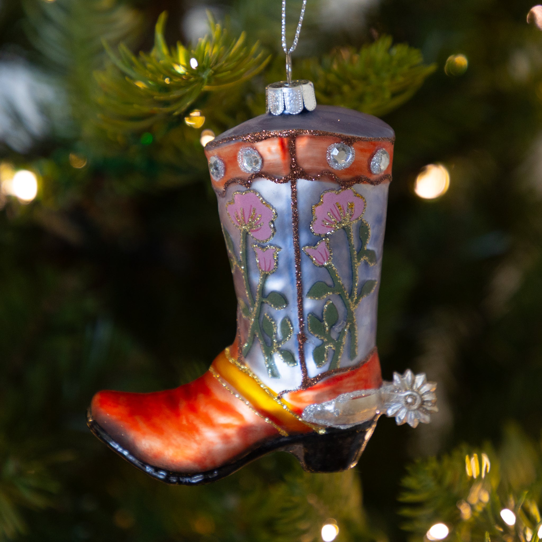 Decorative lavender cowboy boot ornament with a floral design on a Christmas tree.