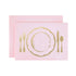 A light pink card with the silhouette of a place setting including a plate and cutlery in solid gold leaf.