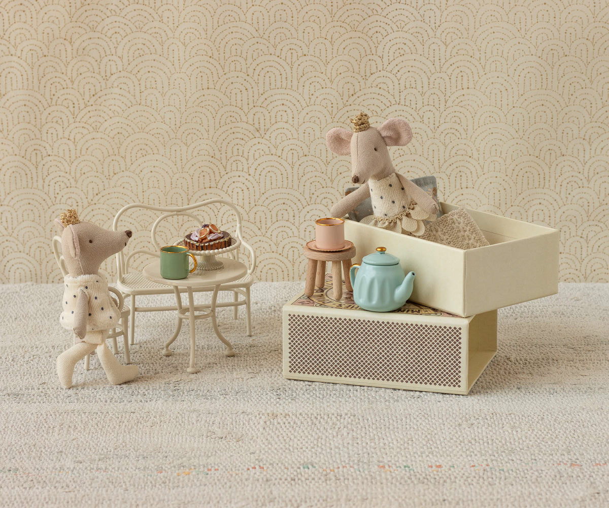 Two toy mice with a miniature tea set on a textured surface with a patterned wall background.