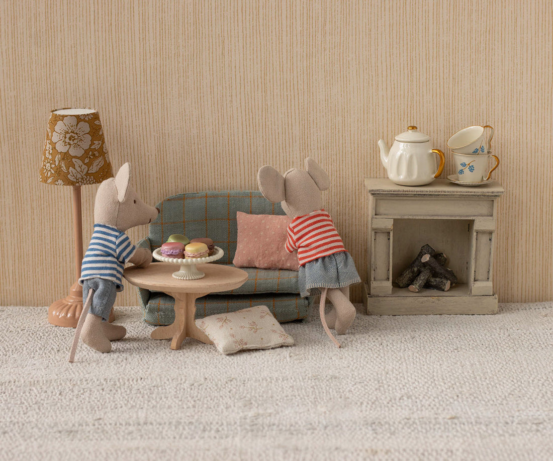 Two toy mice in a miniature living room setting with furniture and decor.