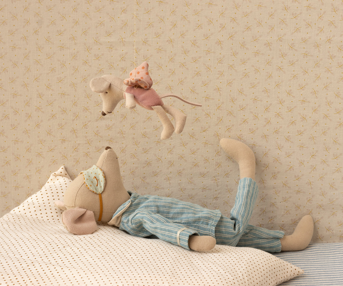 Stuffed animal toy lying on a bed with another toy hanging above against a patterned wall.