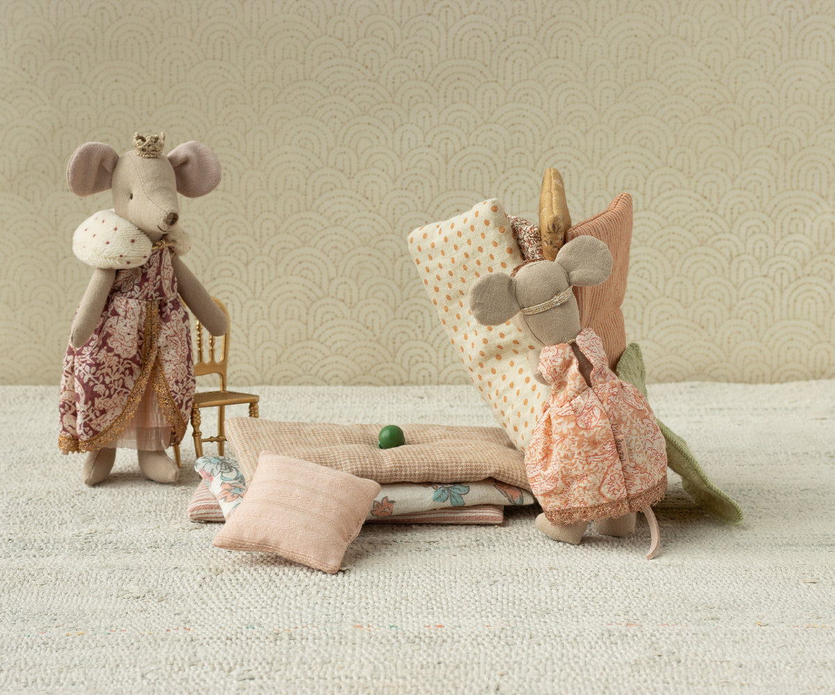 Two plush mouse toys with decorative items on a textured surface and patterned wall background.