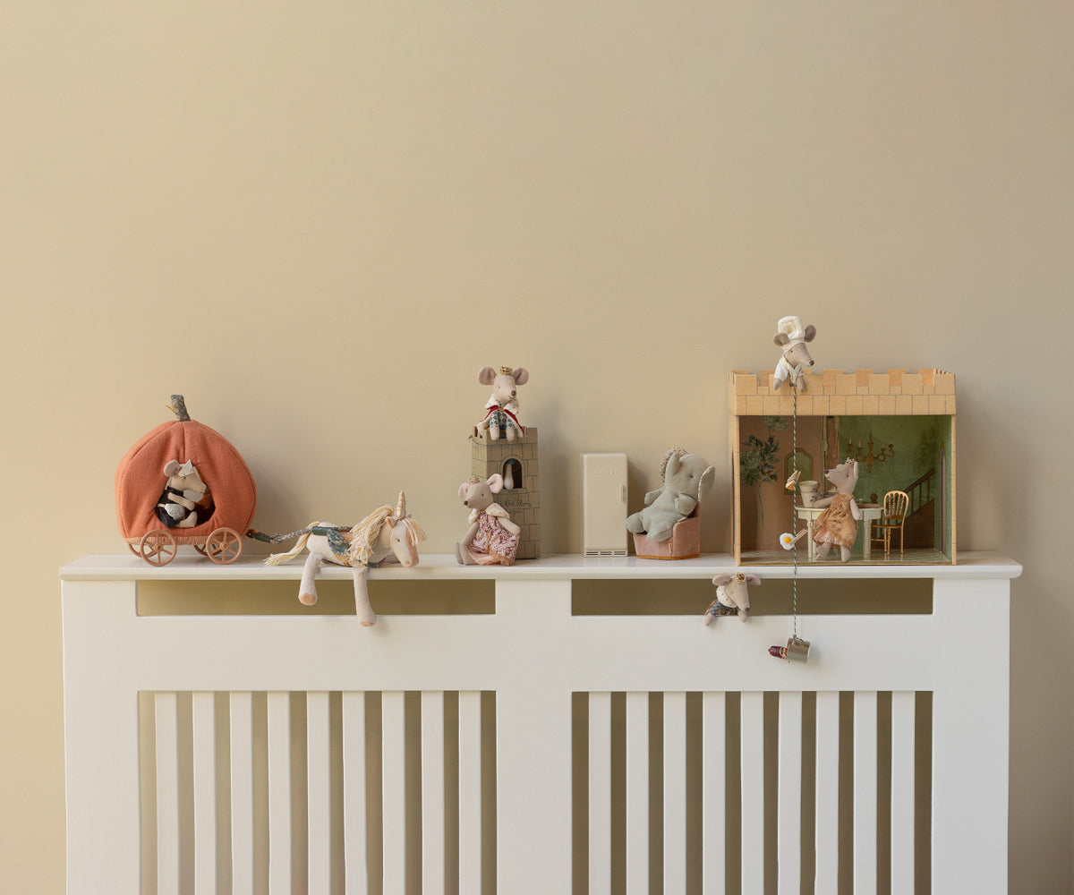 Decorative shelf with small figurines and toys on a white radiator against a beige wall.