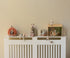 Decorative shelf with small figurines and toys on a white radiator against a beige wall.