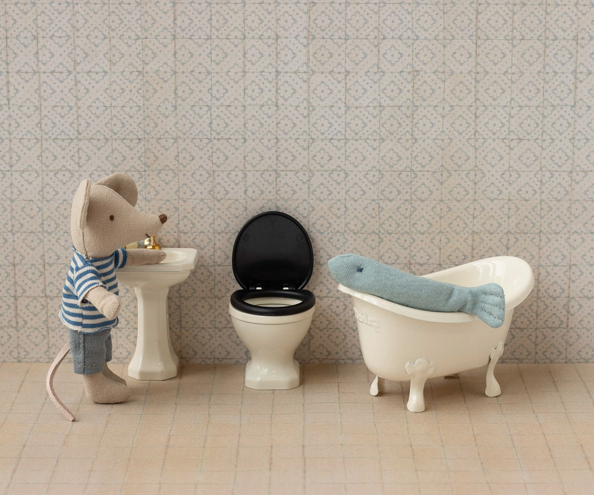 Miniature mouse character by a sink, toilet, and bathtub in a tiled bathroom setting.
