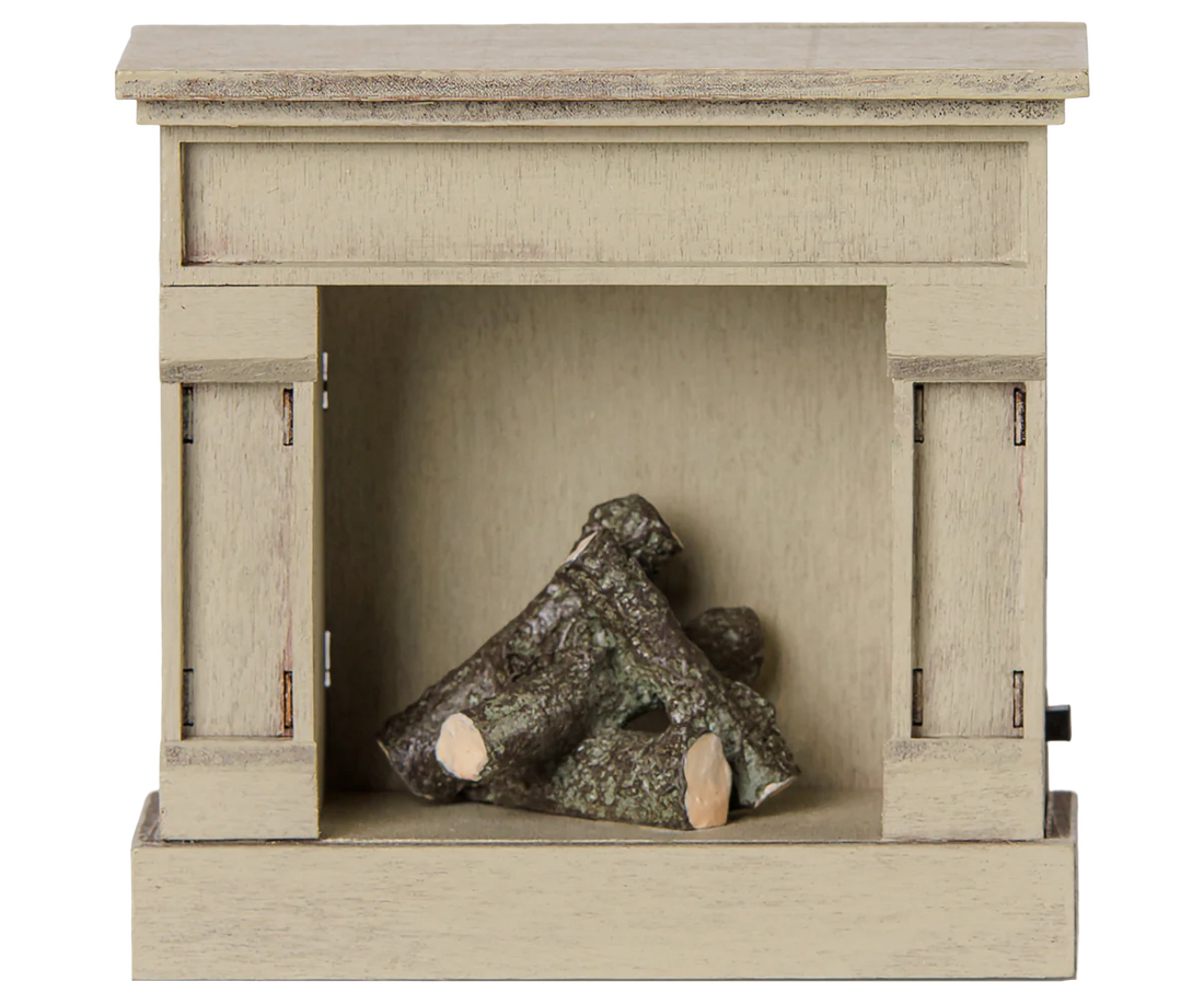 A miniature decorative fireplace figurine in a light beige wood-grain finish, featuring a small pile of faux logs inside the firebox opening, shown against a plain white background.