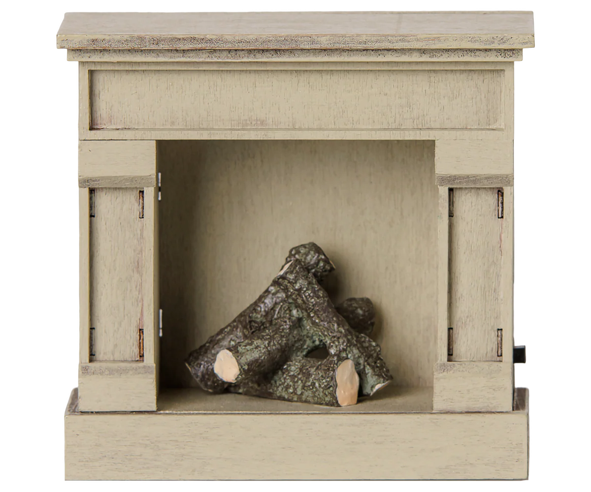 A miniature decorative fireplace figurine in a light beige wood-grain finish, featuring a small pile of faux logs inside the firebox opening, shown against a plain white background.