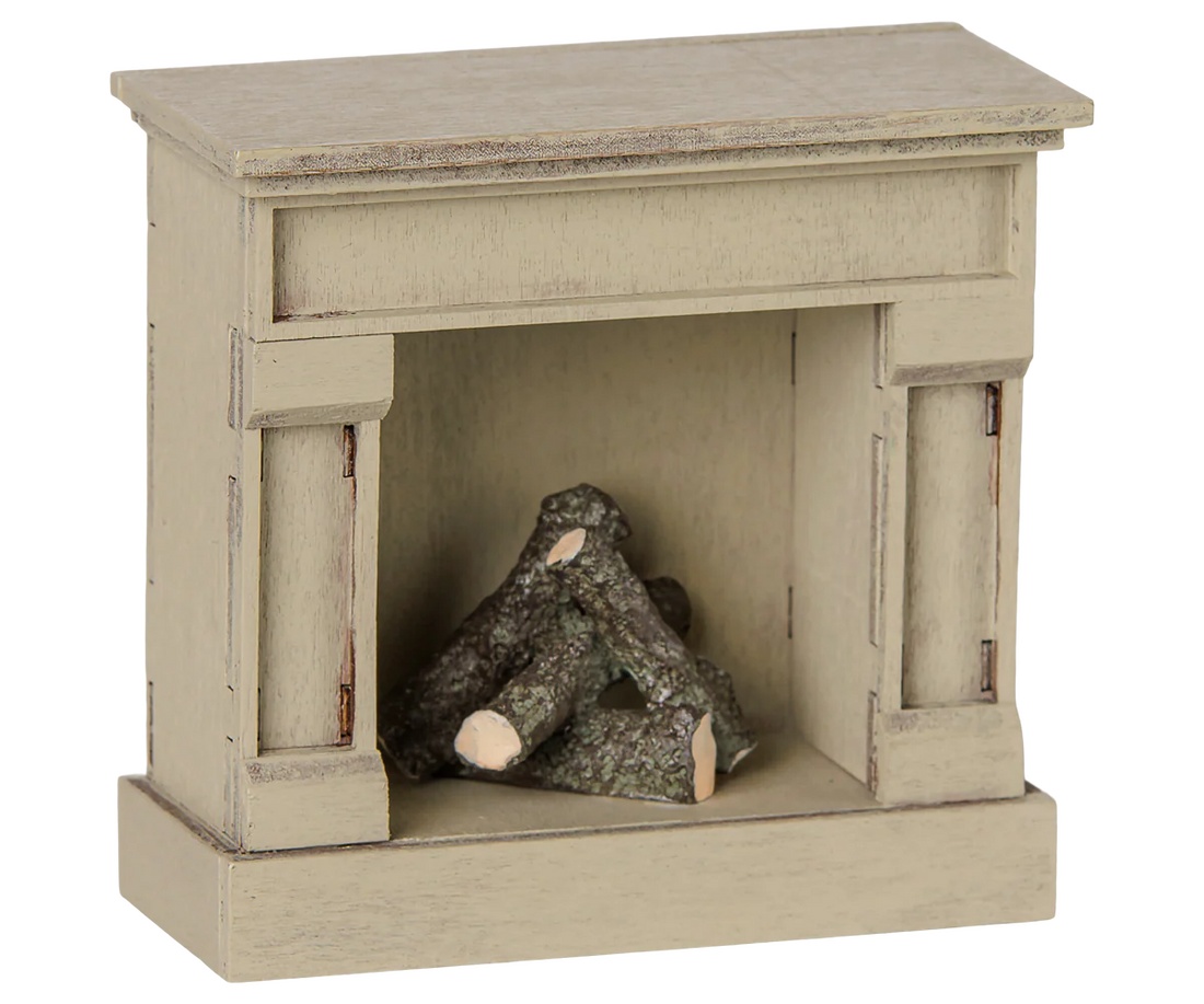 A miniature fireplace mantel figurine in a distressed beige finish, featuring a small stack of faux logs inside the fireplace opening, shown against a plain white background.