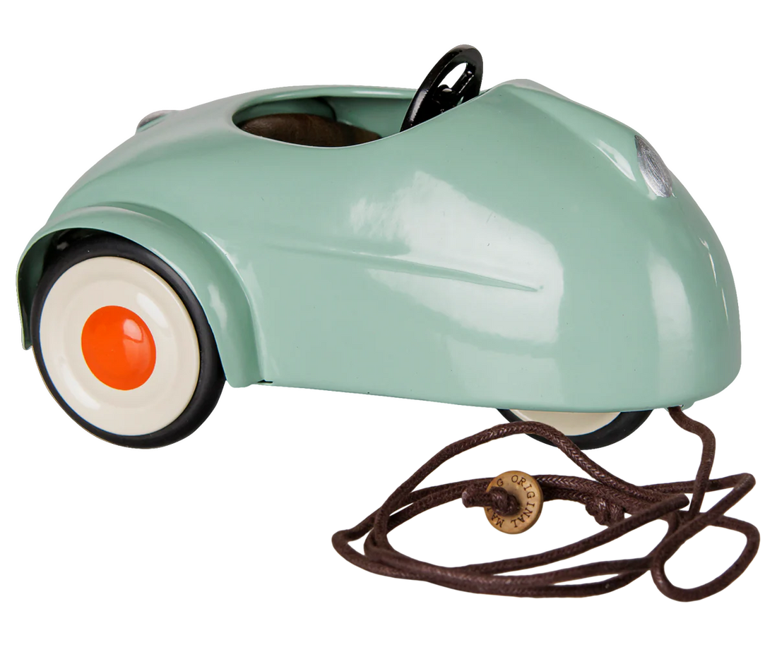 A retro-style miniature toy car in a glossy mint green finish, featuring a black steering wheel, black tires, and white-walled tires with orange center caps, shown on a plain white background.