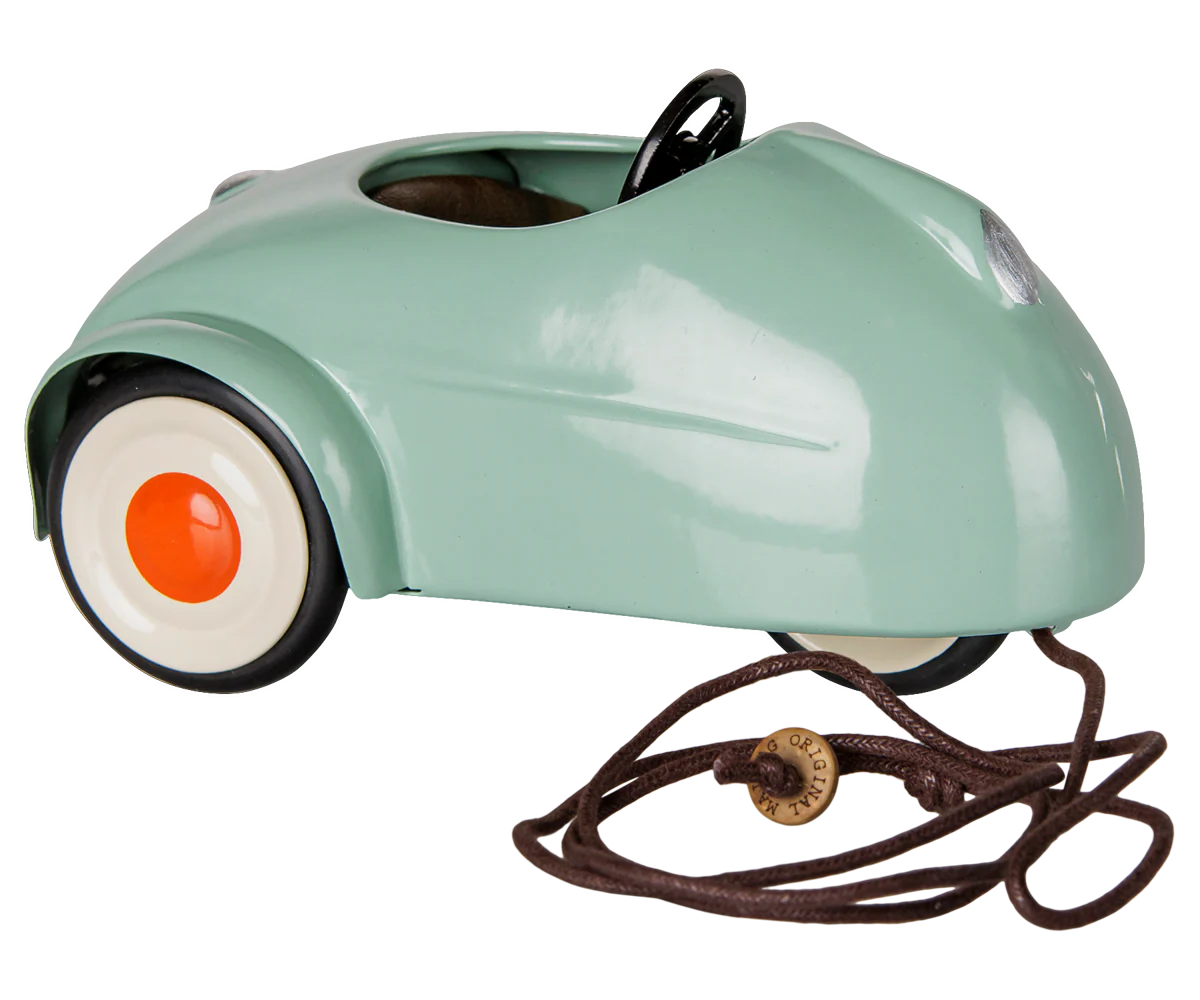 A retro-style miniature toy car in a glossy mint green finish, featuring a black steering wheel, black tires, and white-walled tires with orange center caps, shown on a plain white background.