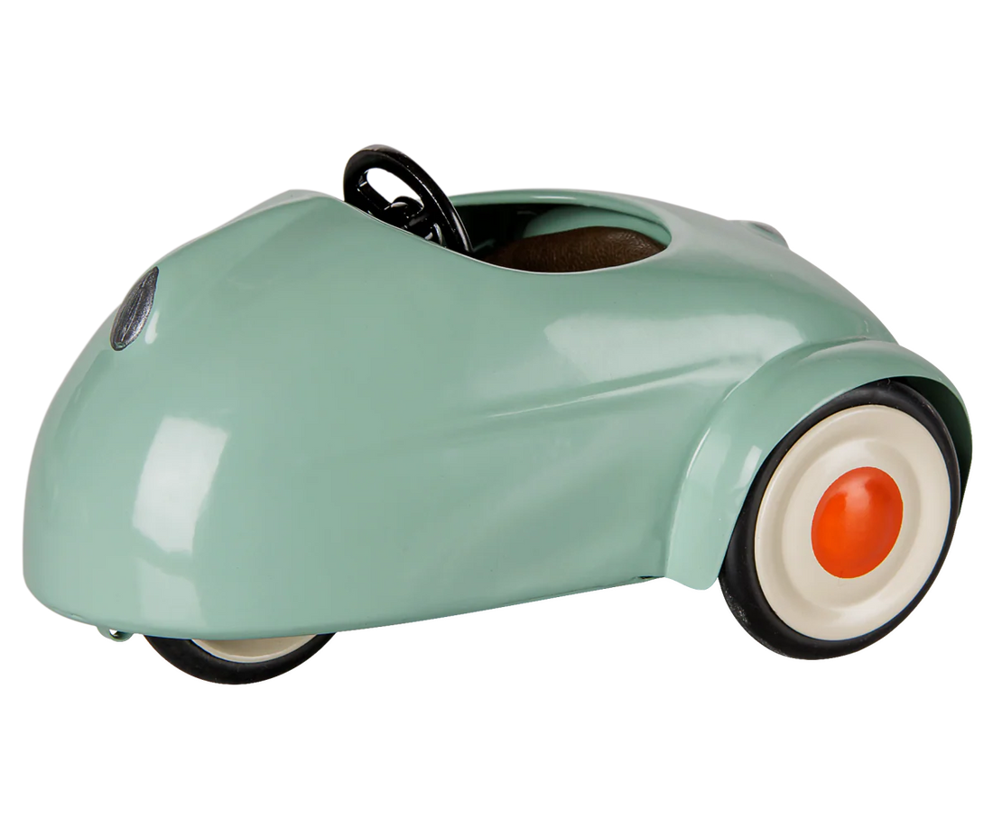 A retro-style miniature toy car in a glossy mint green finish, featuring a black steering wheel, black tires, and white-walled tires with orange center caps, shown on a plain white background.