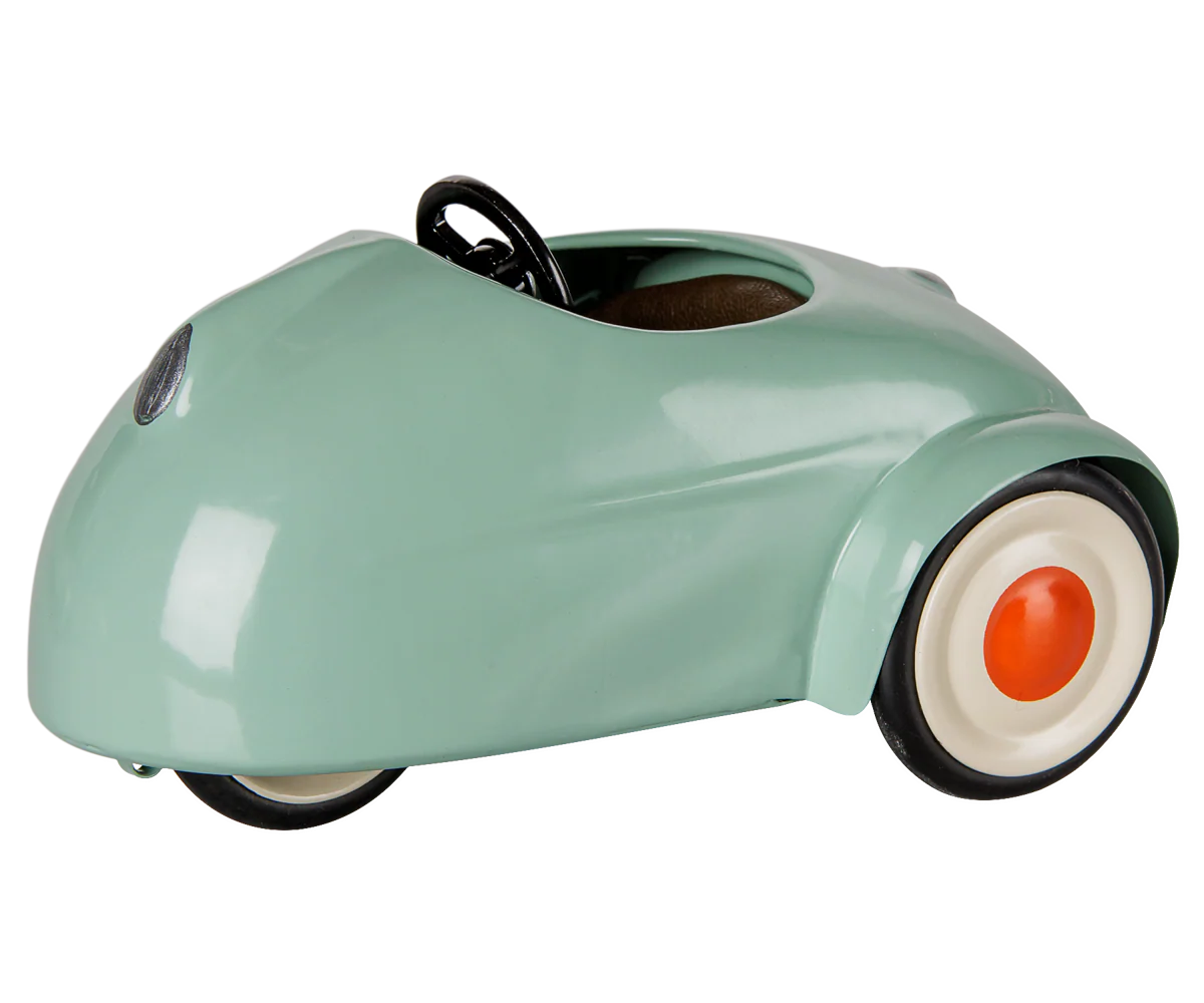 A retro-style miniature toy car in a glossy mint green finish, featuring a black steering wheel, black tires, and white-walled tires with orange center caps, shown on a plain white background.