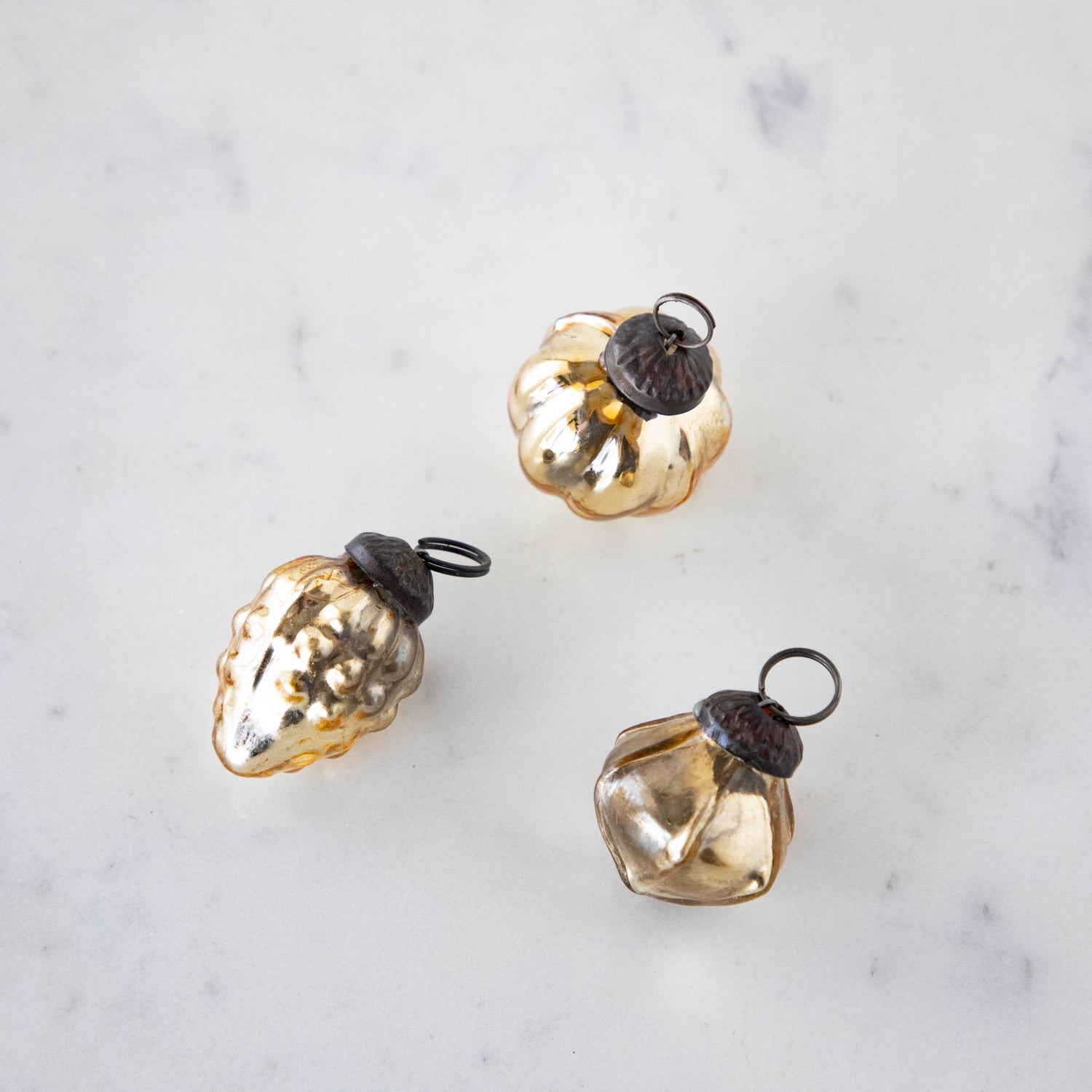 Three various shaped Embossed Antique Gold Mercury Glass Ornaments on a marble table.