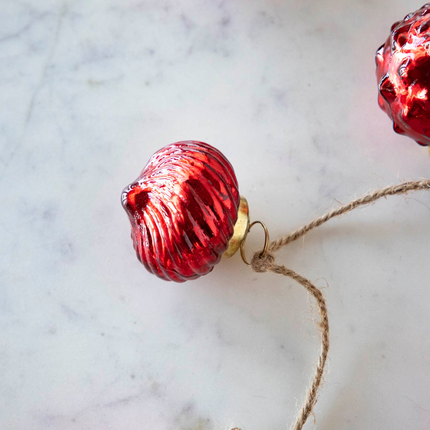 A close up of the Embossed Mercury Glass Ornament Garland showing the lined detailing and jute cord.